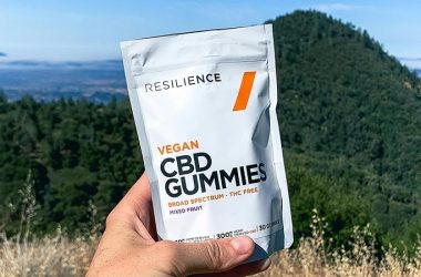 a person's left hand holding a pack of Resilience CBD gummies with a mountain view in the background